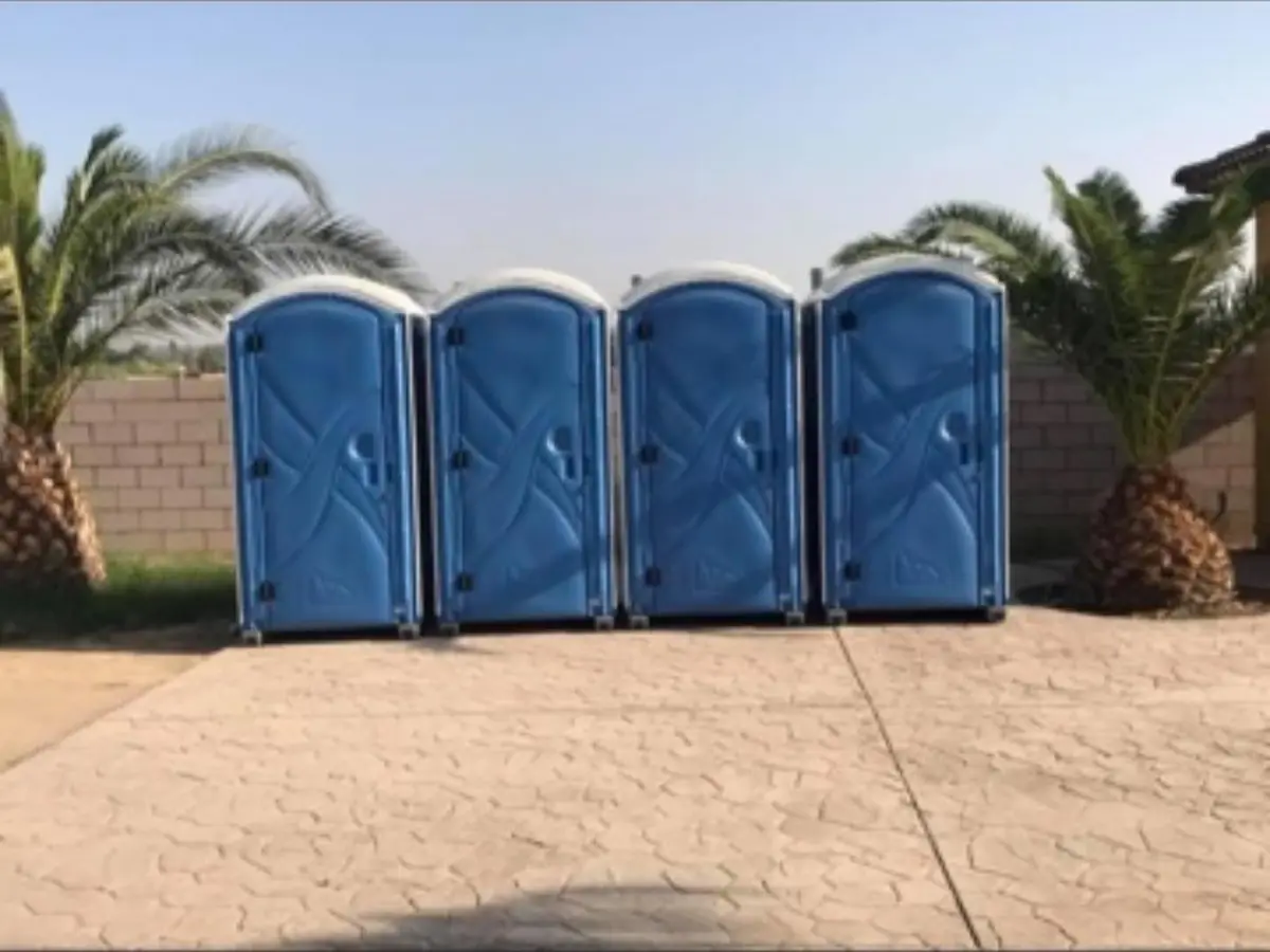 Four blue standard porta potties lined up and ready for an outdoor event